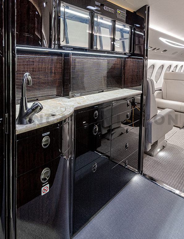 Galley in dark wood tones with granite-look counter in Falcon 7X by Duncan Aviation