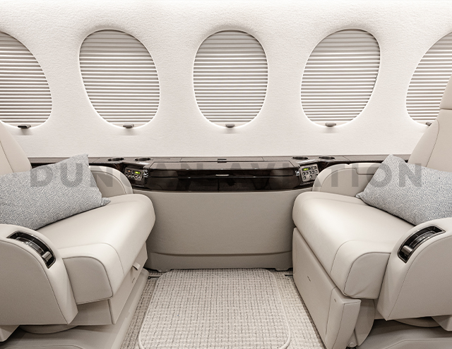 Close up of drinkrail with dark wood accent between two cream leather chairs in refurbished Falcon 7X