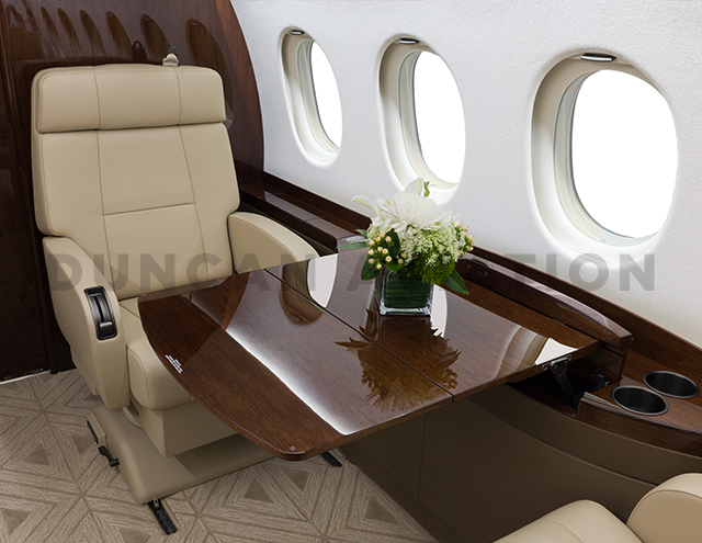 Close up of dark wood pull out table in front of tan leather seat in Falcon 2000 refurbished by Duncan Aviaiton